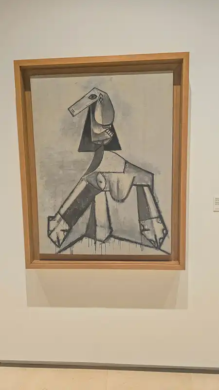 Obraz przedstawiający popiersie kobiety w czerni i bieli (lub szarości) z geometrycznym, kanciastym stylem. Kobieta ma długą, prostokątną głowę i wyraźnie zarysowane ramiona i biust. Linia kroplącego się tuszu widoczna jest na dole.