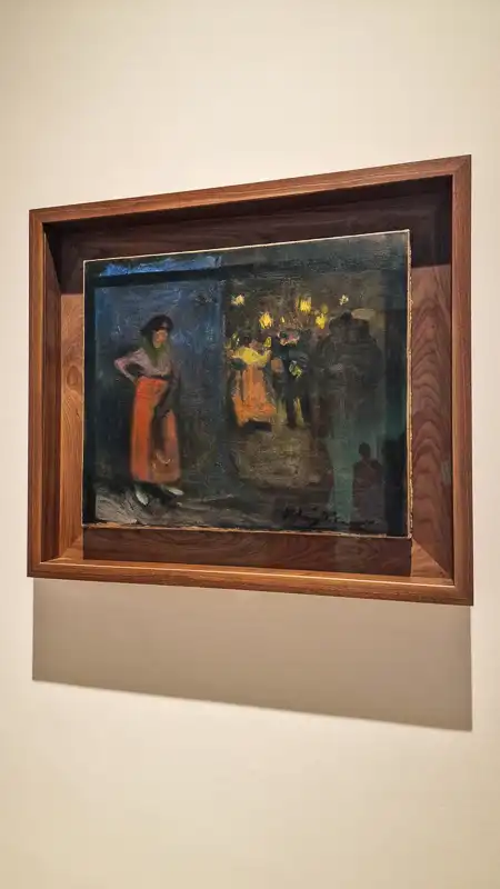 Mały, ciemny obraz w ramie w ciemnym drewnie, przedstawiający scenę nocną. Na pierwszym planie stoi kobieta w pomarańczowej spódnicy, a w tle widać grupę ludzi i rozświetlone lampami wnętrze (może kawiarnia lub scena tańca).